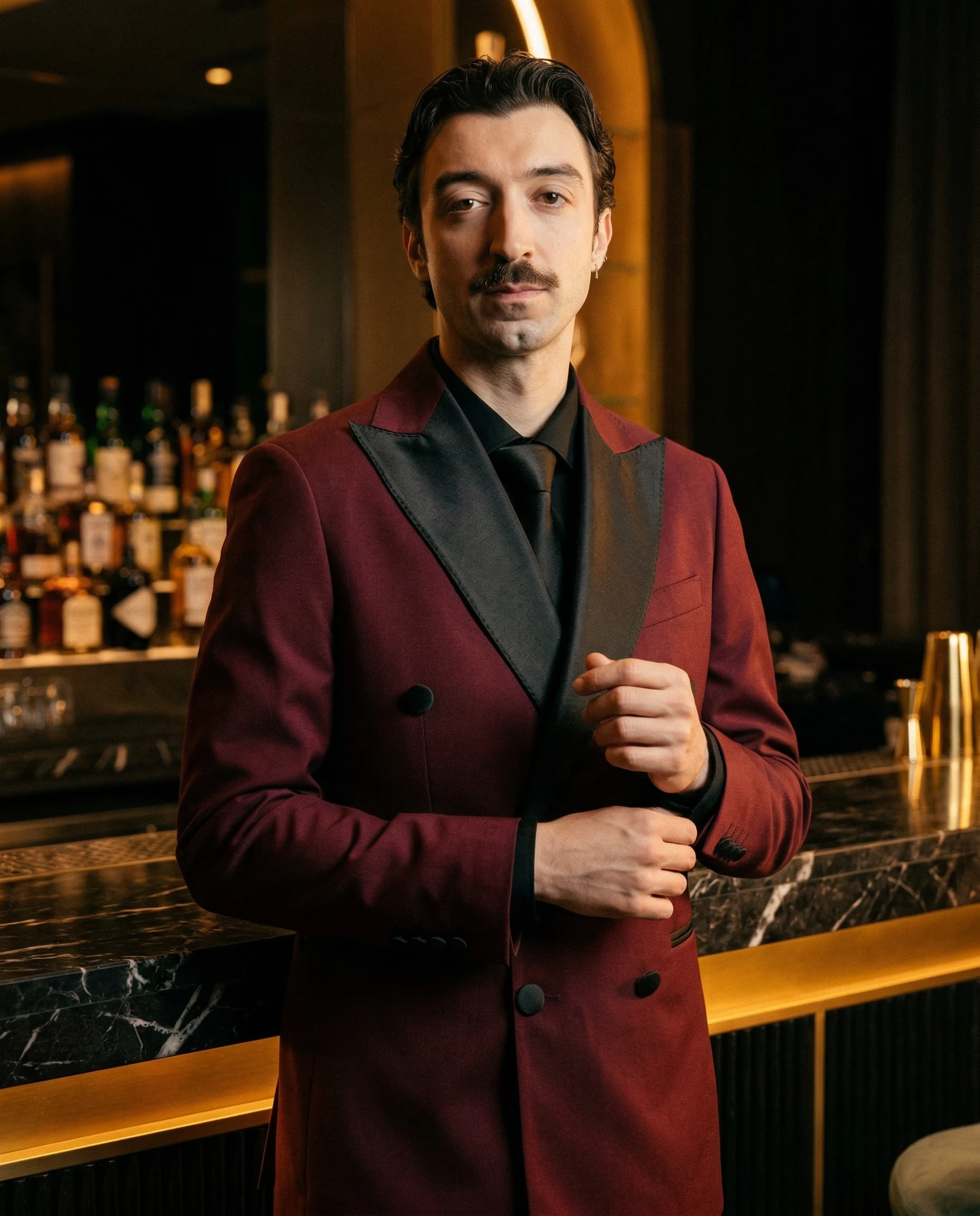 Prima immagine AI: uomo in completo bordeaux con revers scuri davanti a un bar.